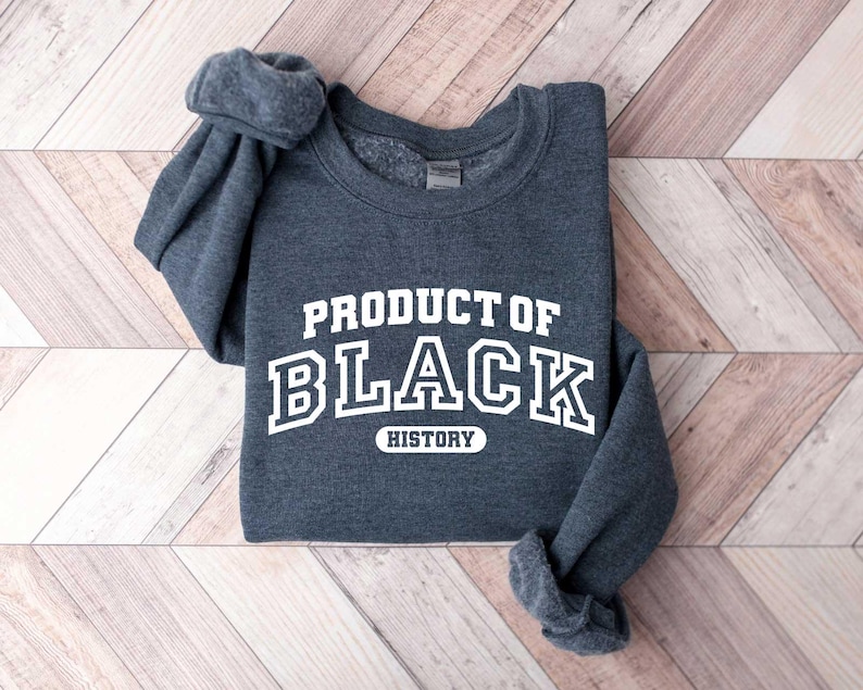 Puede incluir: Una sudadera gris oscura con el texto "PRODUCT OF BLACK HISTORY" en letras blancas.