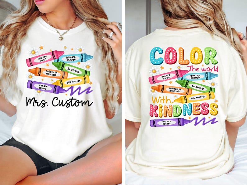 K&ouml;nnte beinhalten: Cremefarbenes T-Shirt mit einem Buntstift-Design und positiven Botschaften. Auf der Vorderseite steht "Mrs. Custom", auf der R&uuml;ckseite "Color the world with kindness". Das T-Shirt hat einen Rundhalsausschnitt und kurze &Auml;rmel.