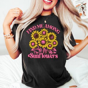 May include: Black t-shirt with a pink and yellow graphic design featuring sunflowers and the text "Find me among the sunflowers".
