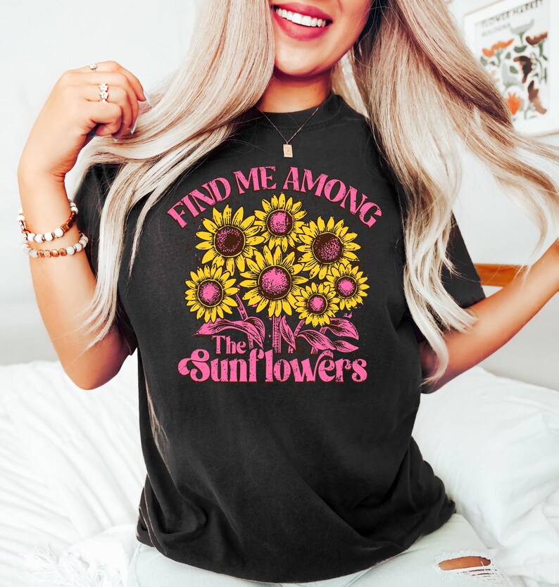 May include: Black t-shirt with a pink and yellow graphic design featuring sunflowers and the text "Find me among the sunflowers".