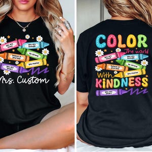 K&ouml;nnte beinhalten: Schwarzes T-Shirt mit einem bunten Buntstift-Design. Die Vorderseite zeigt Buntstifte mit positiven Botschaften und dem Text "Mrs. Custom". Auf der R&uuml;ckseite steht "COLOR the world with KINDNESS."
