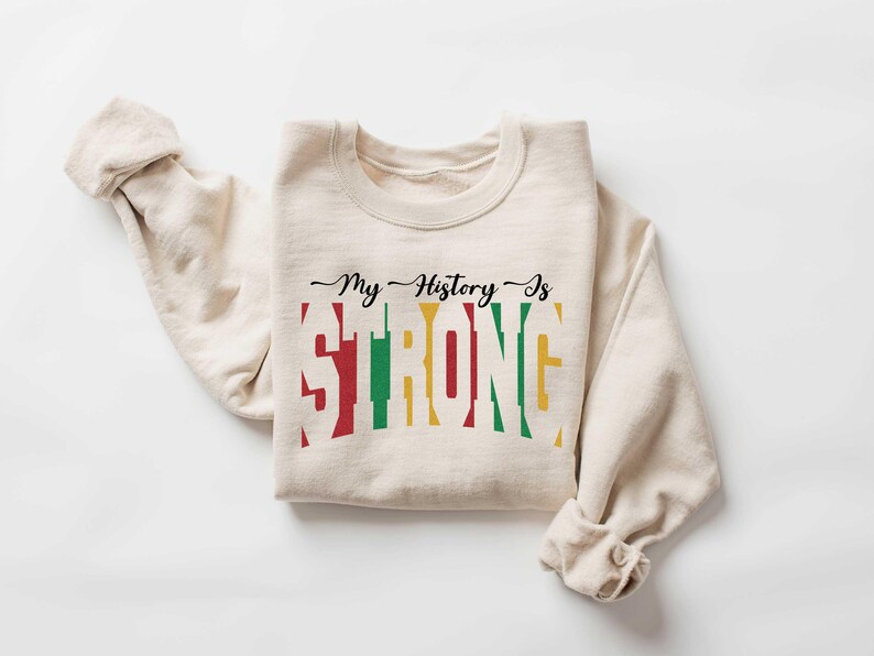 May include: A beige sweatshirt with the text "My History Is Strong" printed in black, red, yellow, and green. The text is styled to look like a stacked bar graph.