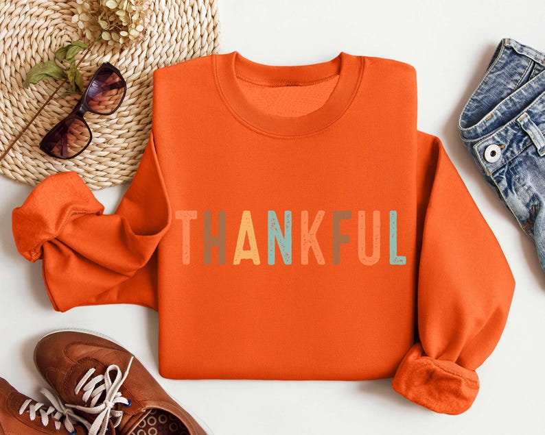 May include: Orange sweatshirt with the word "THANKFUL" printed in colorful letters.