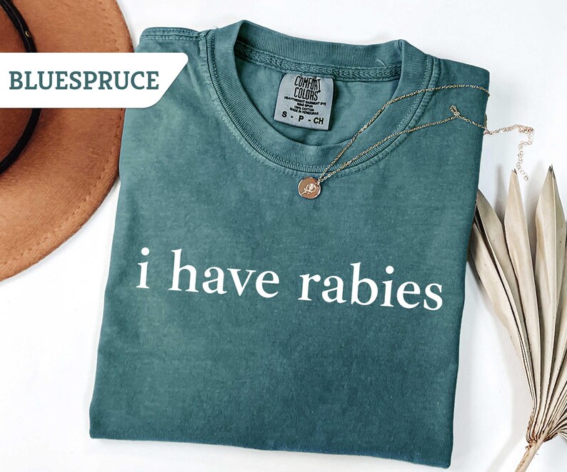 Może przedstawiać: Zielony t-shirt z nadrukiem "i have rabies" w kolorze białym na przodzie.