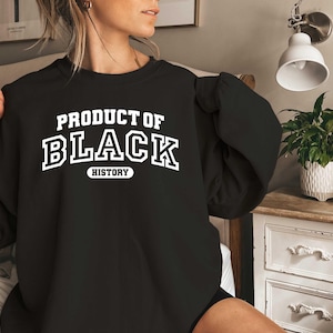 Puede incluir: Sudadera negra con texto blanco que dice "Producto de la historia negra".