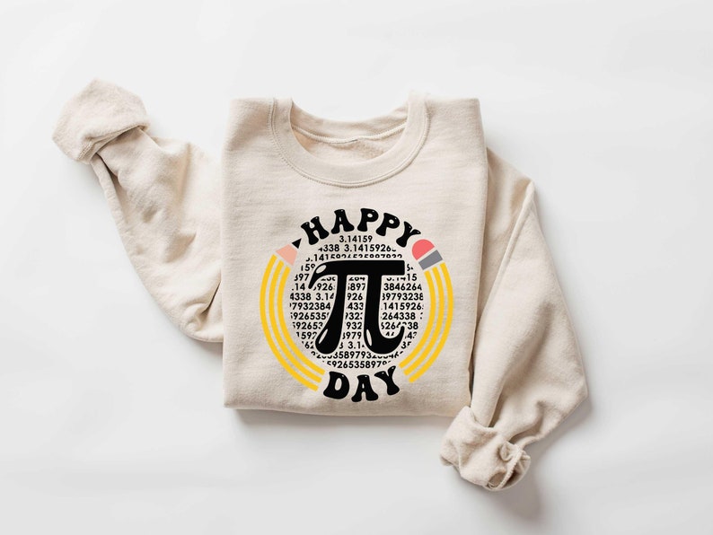 May include: A beige sweatshirt with a black and white graphic design of a circle with the mathematical symbol pi and the text "HAPPY PI DAY" surrounded by yellow and orange stripes. The graphic also includes a pencil with a pink eraser.