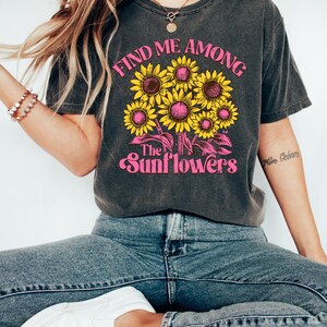 May include: A dark gray t-shirt with a graphic print of sunflowers and the text "Find me among the sunflowers".