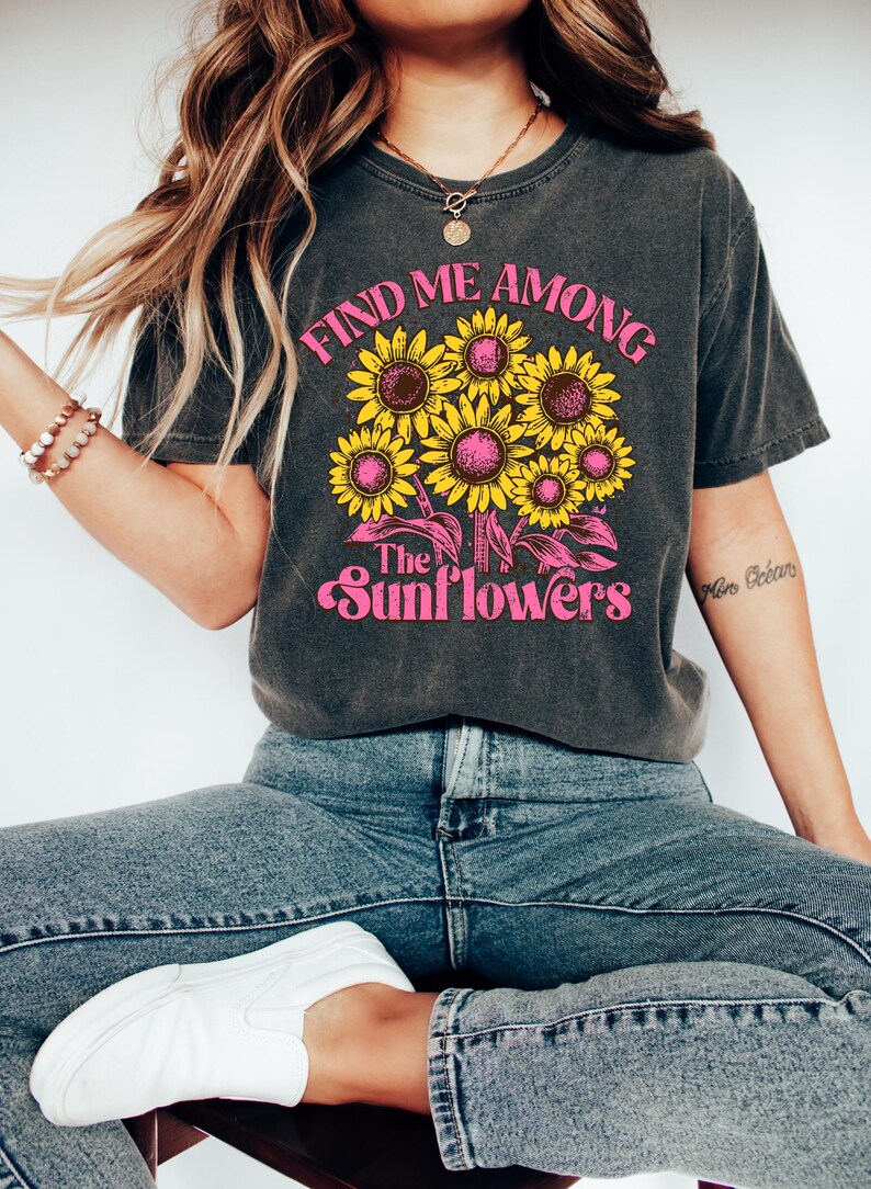 May include: A dark gray t-shirt with a graphic print of sunflowers and the text "Find me among the sunflowers".