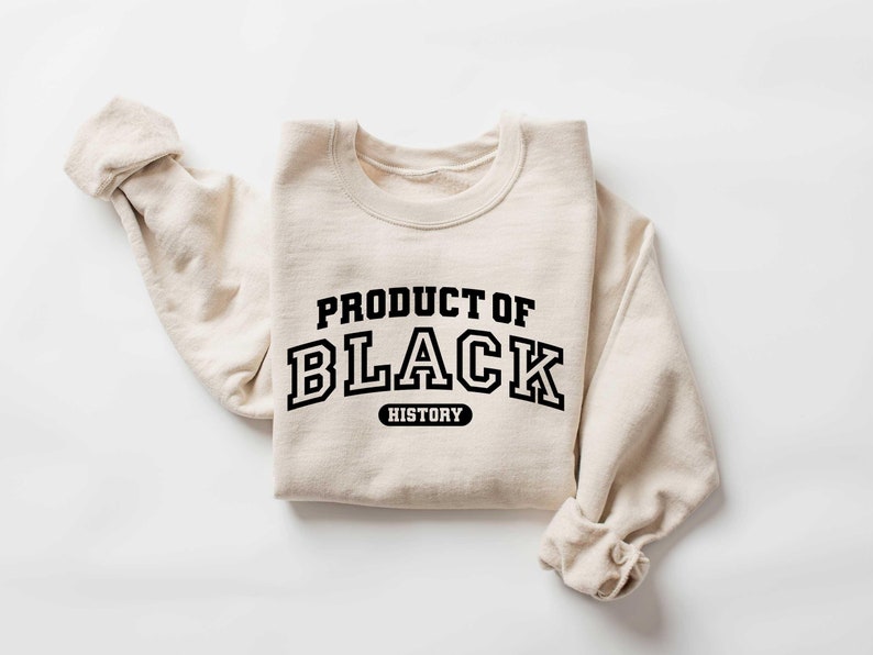Puede incluir: Una sudadera beige con el texto "PRODUCT OF BLACK HISTORY" impreso en negro.
