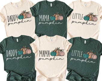 May include: Six t-shirts with pumpkin graphics. The shirts are cream and dark green, with the words "Daddy Pumpkin," "Mama Pumpkin," and "Little Pumpkin" printed on them. Each shirt has a pumpkin graphic in teal, orange, and pink.