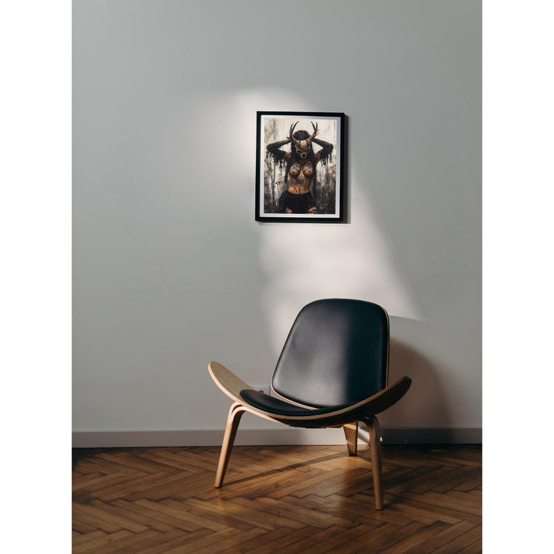 Puede incluir: Una l&aacute;mina de arte enmarcada en negro con una ilustraci&oacute;n oscura y atmosf&eacute;rica de una figura con m&aacute;scara de cornamenta y ropa desgarrada, situada sobre un sill&oacute;n de cuero negro con estructura de madera curvada sobre suelo de espiga.