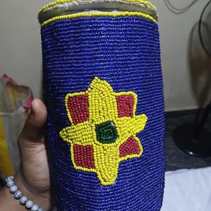 May include: A blue beaded container with a yellow and red flower design. The container has a white lid.