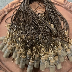 Puede incluir: Un grupo de pequeñas botellas de vidrio con tapones de corcho y un collar de cordón marrón. Las botellas están llenas de un polvo marrón claro.