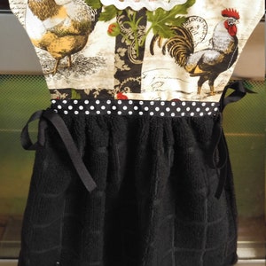 May include: A black and white checkered kitchen towel with a black ribbon and white polka dots. The top of the towel is made of fabric with a rooster and floral pattern. The fabric has the text "Bologna" and "France" printed on it.