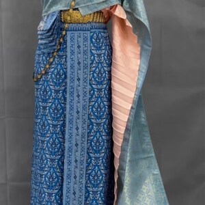 May include: A blue and white patterned skirt with a gold belt and a light blue shawl with a gold necklace. The shawl has a pink lining.