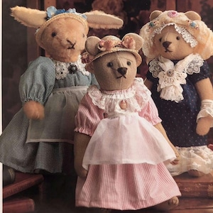 May include: Three plush dolls: a rabbit and two bears, each wearing vintage-style clothing. The rabbit has long ears and a blue and white checkered dress. The bears wear dresses and hats with lace and floral accents, evoking a nostalgic, handcrafted aesthetic.