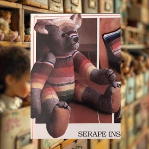 Könnte beinhalten: Ein handgefertigter Teddybär mit einem gestreiften Design in Rot-, Orange-, Gelb-, Grün- und Blautönen. Der Bär hat braune Pfoten und eine passende Nase. Der Text "SERAPE INS" ist unten im Bild zu sehen. Der Bär sitzt.