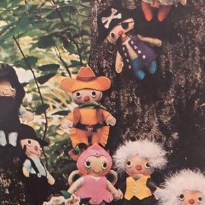 May include: A selection of handmade felt dolls, each with distinctive outfits and features. The dolls are attached to a tree trunk, displaying a variety of characters, including a cowboy, a pirate, and a soldier. The dolls are colourful and whimsical.