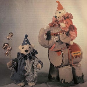 May include: A whimsical image features two teddy bears dressed as clowns. One bear holds balloons, while the other rides a gray elephant. The elephant has a red saddle and decorative details. The bears wear blue and red clown outfits with matching hats.