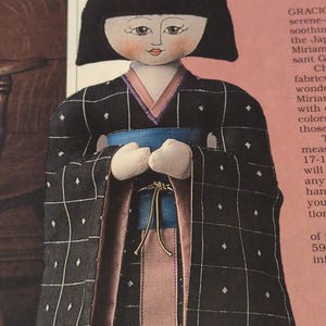 Puede incluir: Mu&ntilde;eca hecha a mano con un kimono negro con un patr&oacute;n de cuadr&iacute;cula blanca y peque&ntilde;os diamantes blancos. El kimono tiene un forro rosa y azul, y una faja azul. La mu&ntilde;eca tiene un peinado bob negro y una cara pintada.