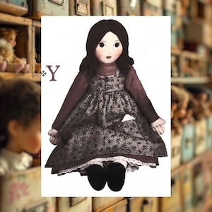 Peut inclure: Une poupée de chiffon faite à la main avec des cheveux noirs, vêtue d'une robe à imprimé floral foncé sur une chemise bordeaux à manches longues. La poupée a une poche blanche et une bordure en dentelle blanche. Des chaussures noires complètent le look. La lettre "Y" est visible.