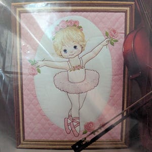 May include: A crewel embroidery kit titled 1615 Tiny Ballerina 11" x 14". The image features a blonde ballerina in a pink tutu and ballet slippers, wearing a floral crown and holding pink roses, set against a quilted pink background.