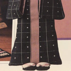 Puede incluir: Mu&ntilde;eca con un kimono negro con un patr&oacute;n de cuadr&iacute;cula blanca y peque&ntilde;os acentos de diamantes blancos. La t&uacute;nica tiene un panel central de color malva y se combina con zapatillas a juego. El atuendo de la mu&ntilde;eca recuerda la vestimenta tradicional japonesa.