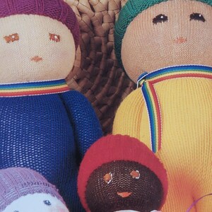 May include: A collection of handmade knitted dolls. The dolls have round faces with embroidered features and wear colorful knitted hats and outfits. Each doll has a rainbow-striped collar. The dolls are in shades of blue, yellow, red, and purple.
