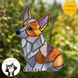 May include: Stained glass corgi dog suncatcher with a copper-colored frame. The dog is in a sitting position and features shades of blue, orange, and purple glass. The suncatcher has a Hobby License logo and a Charming Glass Co. logo.