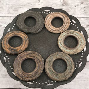 May include: Six ceramic rings with a textured, swirled design in shades of brown, beige, and blue. The rings are arranged in a circle on a black, decorative plate.