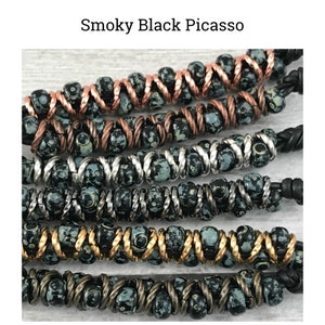May include: A close-up of a multi-strand bracelet with black and white beads. The beads are interspersed with copper, silver, and gold wire. The bracelet is made with a variety of materials and has a unique, handcrafted look.