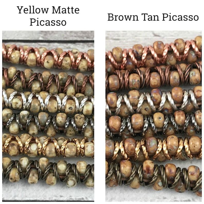 May include: Close-up of two strands of beads, one in a yellow matte Picasso color and the other in a brown tan Picasso color. Both strands feature a mix of copper, silver, and gold wire accents.