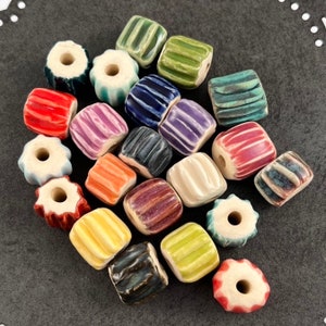 May include: A collection of 18 ceramic beads in various colors and patterns. The beads are all square shaped and have a hole in the center. The beads are perfect for jewelry making or other craft projects.