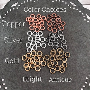 May include: Assortment of small, twisted metal rings in copper, silver, and gold. The rings are labeled "Copper", "Silver", and "Gold" with the words "Bright" and "Antique" below.  The rings are for jewelry making.