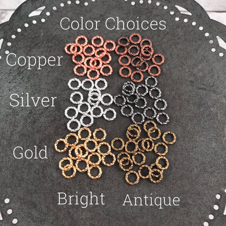 May include: Assortment of small, twisted metal rings in copper, silver, and gold. The rings are labeled "Copper", "Silver", and "Gold" with the words "Bright" and "Antique" below.  The rings are for jewelry making.