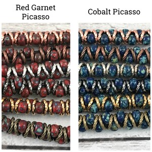 May include: Two strands of multi-colored beads, one red and one blue, with copper, silver, and gold accents. The red strand is labeled "Red Garnet Picasso" and the blue strand is labeled "Cobalt Picasso".