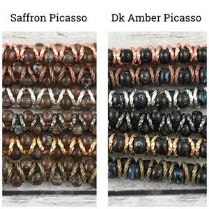 May include: Two rows of colorful glass beads, each row with a different color and pattern. The top row is copper and brown, the second row is silver and brown, the third row is gold and brown, and the bottom row is bronze and brown. The beads are arranged in a repeating pattern of alternating colors. The image is labeled "Saffron Picasso" and "Dk Amber Picasso".