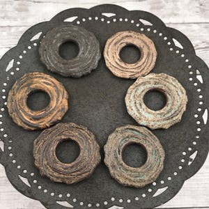 May include: Six ceramic rings with a swirl design in various shades of brown, black, and blue. The rings are arranged in a circle on a black background.