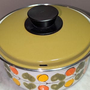 May include: A vintage white enamel pot with a yellow-green lid and a black handle. The pot features a decorative pattern of orange and yellow fruit and green leaves. The pot is a classic kitchenware item.