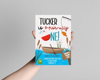 Peut inclure: Une invitation d'anniversaire sur le thème de la pêche. Le texte dit "Tucker is o-fish-ally ONE !" avec une illustration d'un flotteur, d'un poisson et d'un bateau. L'invitation comprend les détails de l'événement : date, heure et lieu.