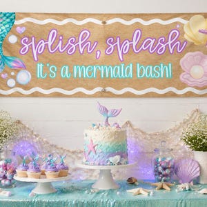 May include: A mermaid-themed party banner with the text "splish, splash, it's a mermaid bash!" is displayed above a table decorated with a cake, cupcakes, and balloons. The banner features a mermaid tail and other aquatic elements.