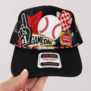 May include: A black trucker hat featuring a foam front with a sticker reading OTTO WORLD FAMOUS FOAM FRONT OSFM TRUCKER. The hat is decorated with patches including a baseball, a red star, a number one foam finger, and a red and white checkered flag.