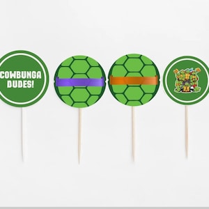 Puede incluir: Cuatro adornos para cupcakes verdes con bordes blancos. Uno tiene el texto "COWABUNGA DUDES!" en blanco. Dos tienen un diseño de caparazón de tortuga verde con bandas moradas y naranjas. El último presenta a las Tortugas Ninja.
