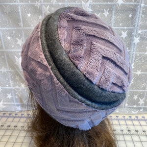 May include: A purple and gray fuzzy hat with a quilted design. The hat is made of soft, plush fabric and has a simple, classic style.