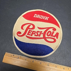 May include: Embroidered Pepsi-Cola patch with a red, white, and blue design. The circular patch features the Pepsi-Cola logo in red script, with the word "DRINK" above. The patch is approximately 4 inches in diameter.