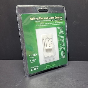 Puede incluir: Un control de ventilador de techo y luz en un embalaje de plástico transparente. El embalaje verde y blanco presenta el texto "Ceiling Fan and Light Control" y la marca "Hunter". La unidad de control blanca tiene un interruptor y ajustes numerados.