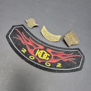 Puede incluir: Una colección de parches y pines con temática de motocicletas. El parche principal es negro con llamas rojas y el texto "KTC 2002". Hay tres pines dorados con el texto "HPC" y un pin curvo con el texto "HPC".