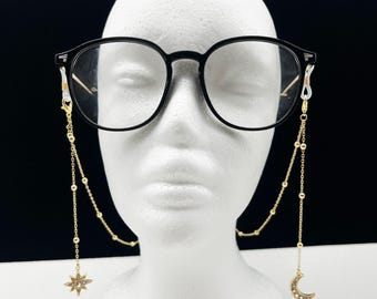 May include: Gold eyeglasses chain with a star and crescent moon charm. The chain is made of small gold beads and has a simple design.
