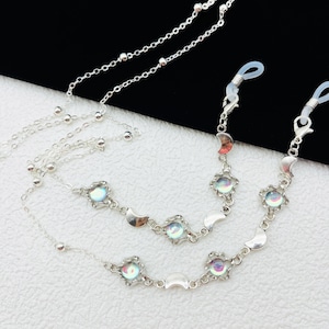May include: A silver chain with iridescent moon and star charms. The chain has two clasps for attaching to glasses.