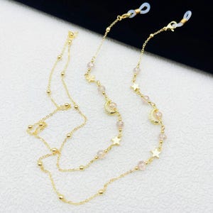 Könnte beinhalten: Goldene Brillenkette mit durchsichtigen Perlen und Sternen- und Halbmond-Anhängern.